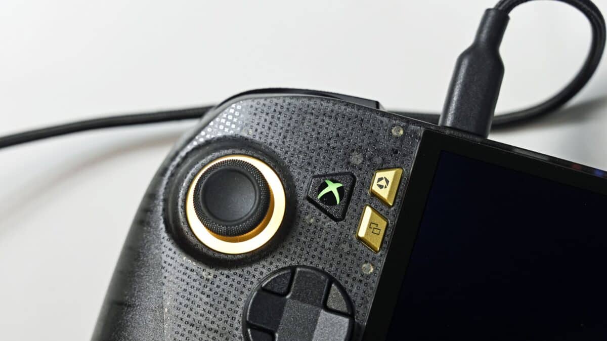 Close-up of the ROG Ally X20 left grip with dbrand skin, illuminated joystick ring, and glowing green Xbox guide button